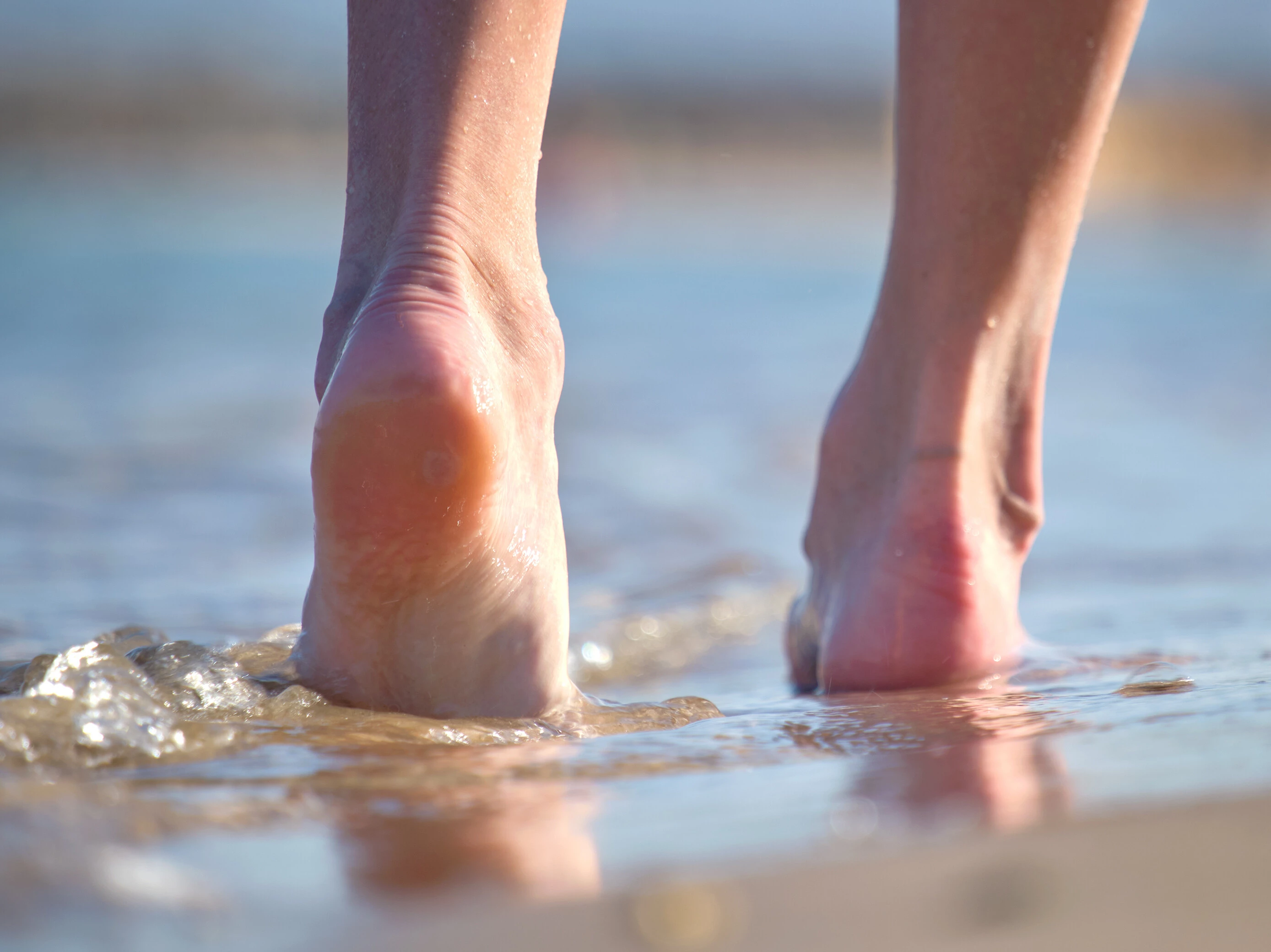 Zwei Füße am Strand gehen im Wasser